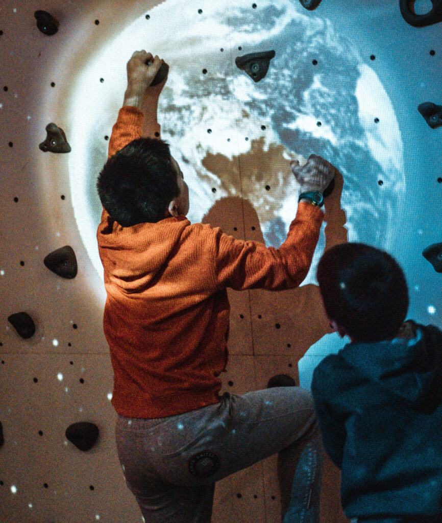 Enfant escalade un mur avec motif planète Terre.
