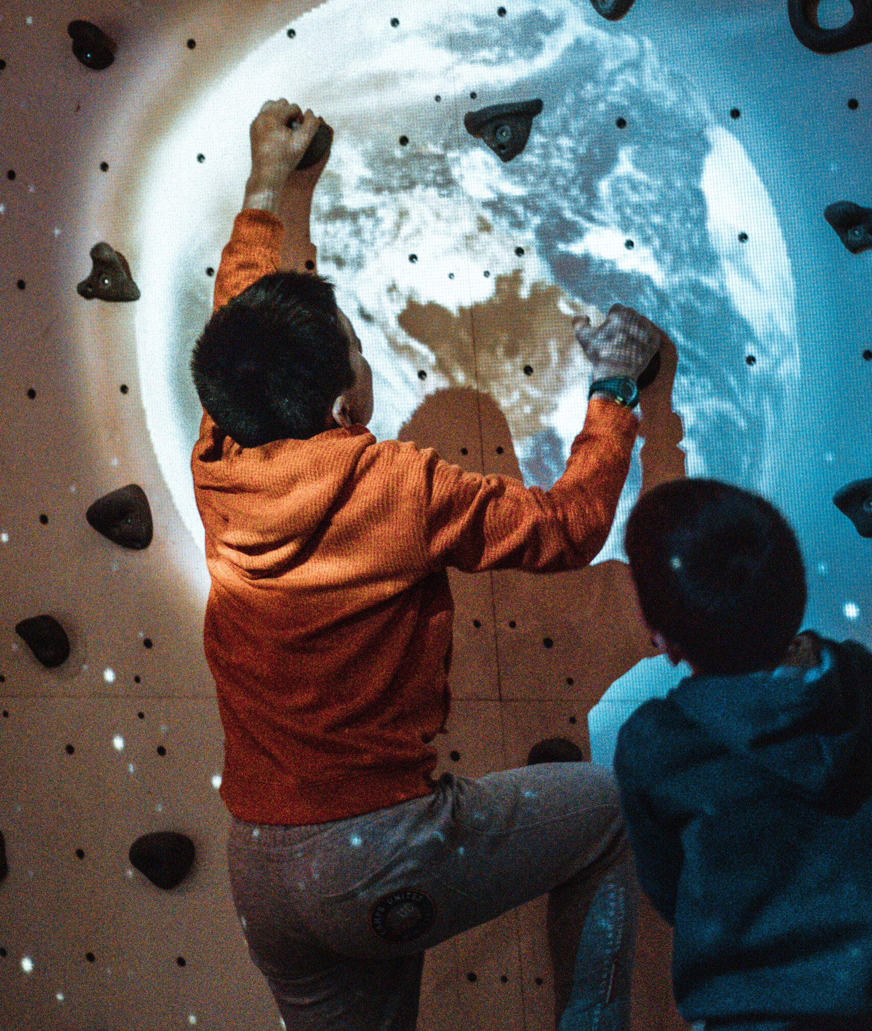 Enfant escalade un mur avec motif planète Terre.