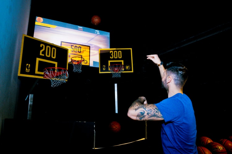 Homme jouant au basket intérieur, trois paniers visibles.