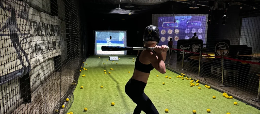 Femme jouant au baseball intérieur avec écran de simulateur.